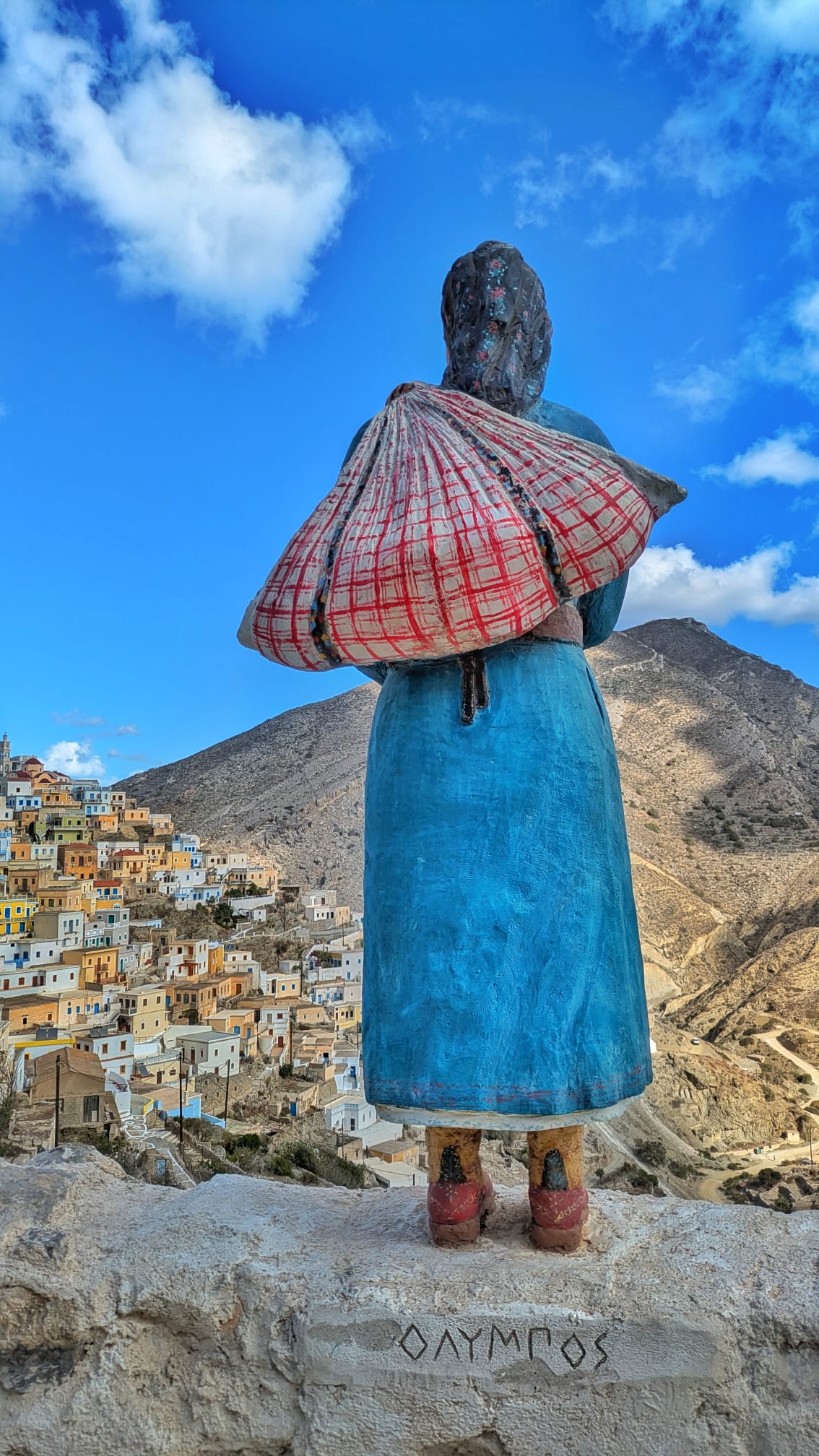 Statua di donna in costume tradizionale con vista sul villaggio di Olympos